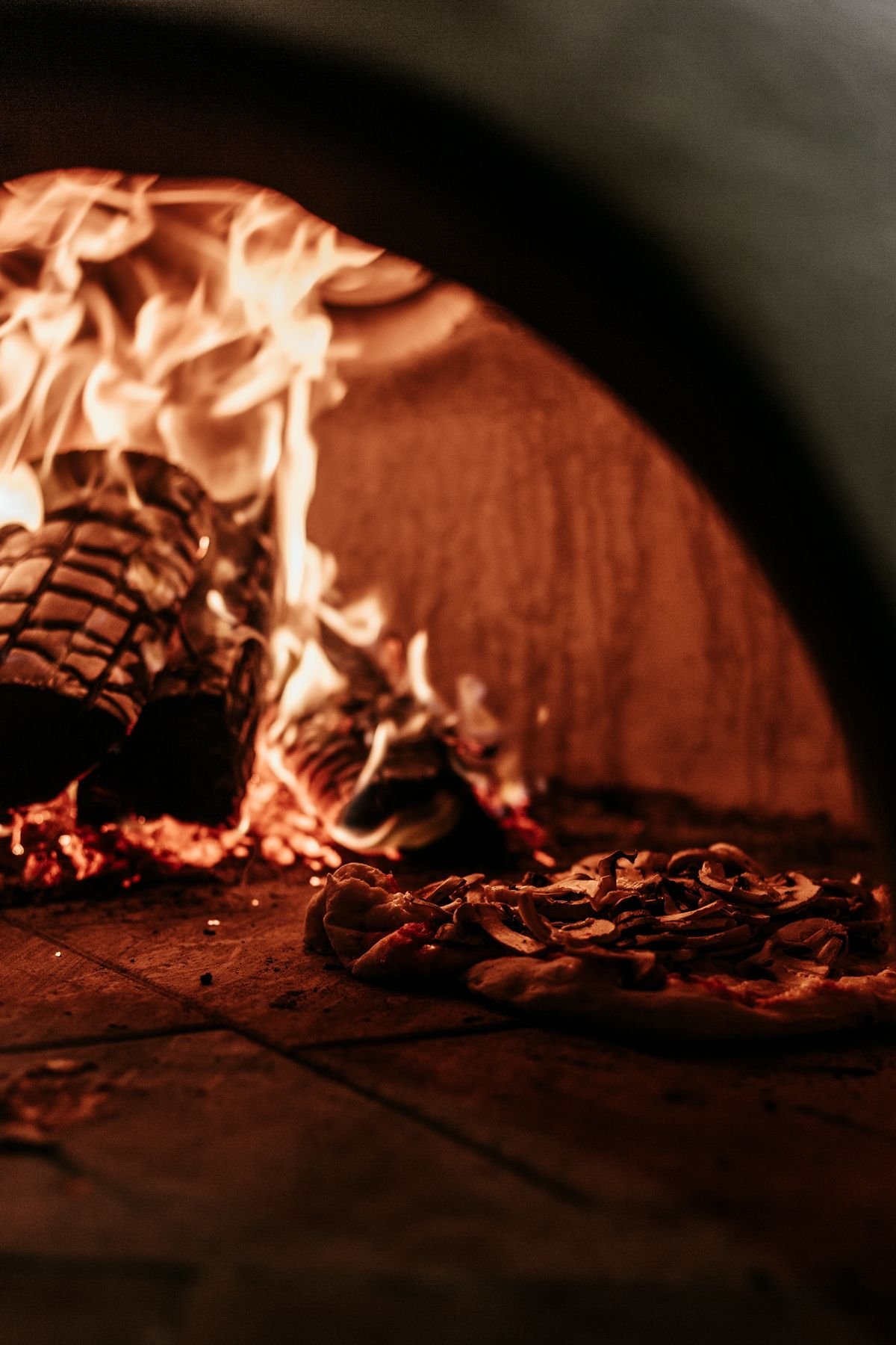 Pizza baking beside the flames of a wood-fired oven