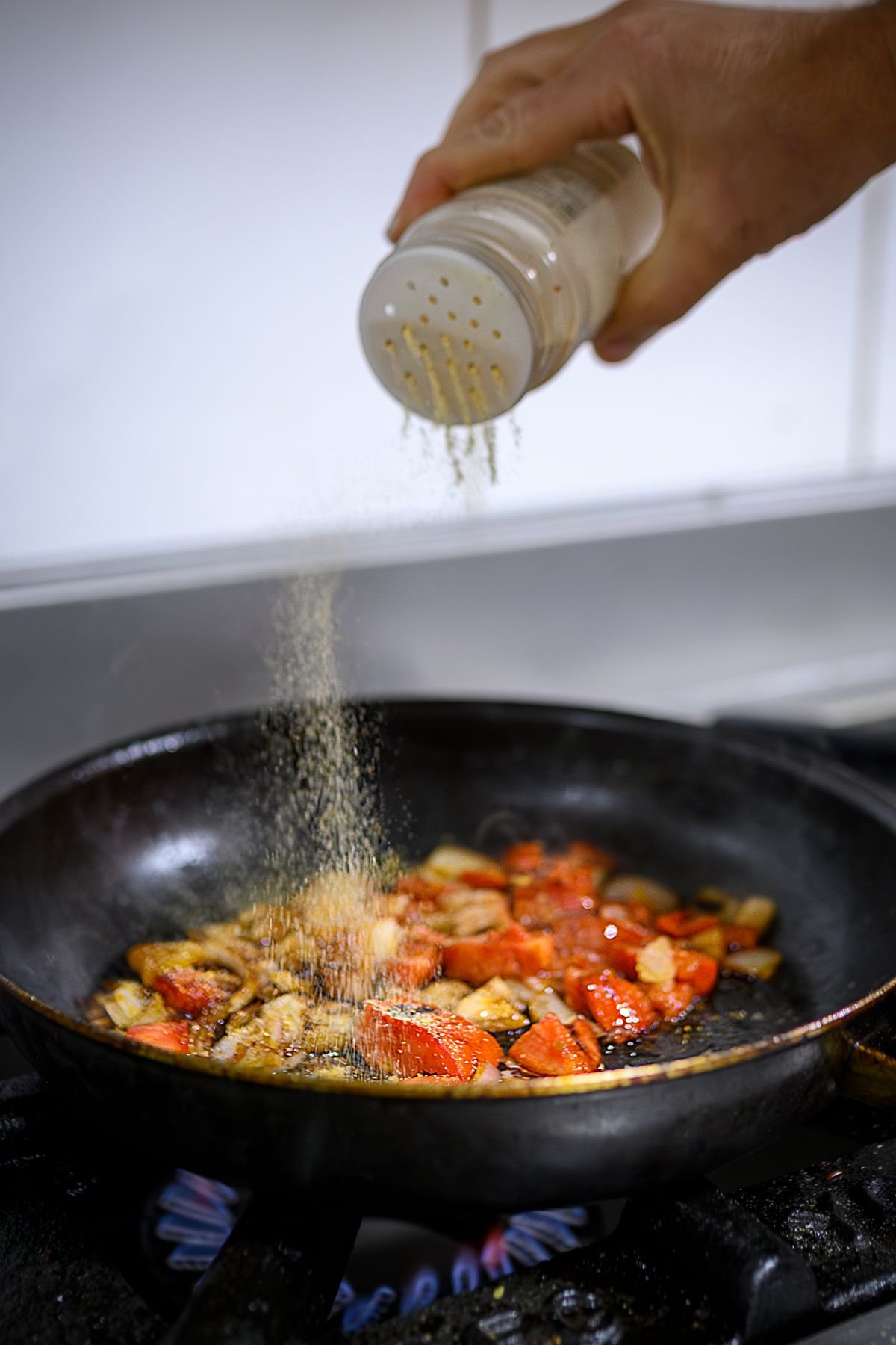 A cook seasoning sauteed vegetables in a skillet